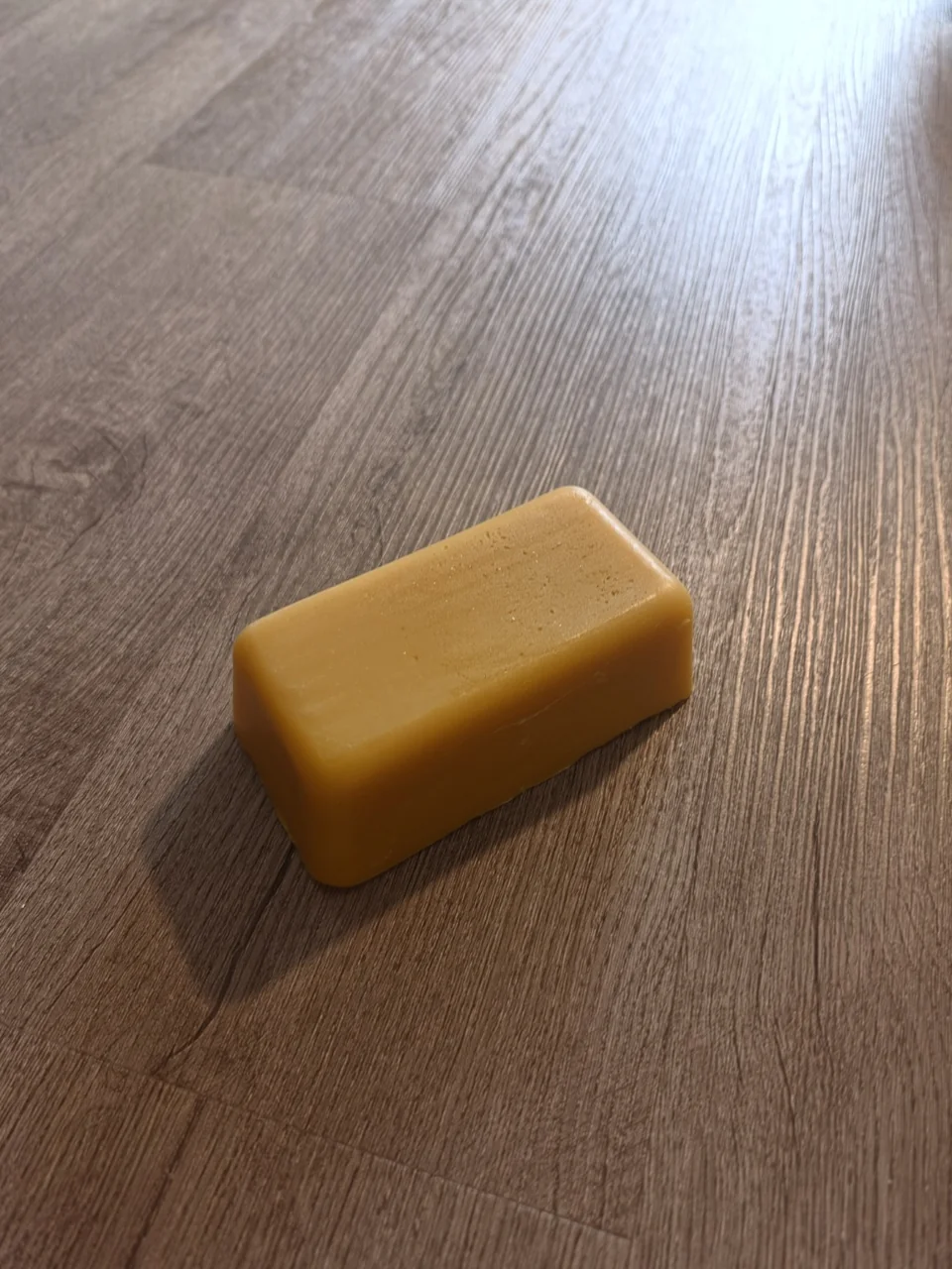 A rectangular yellow beeswax bar on a wooden surface.