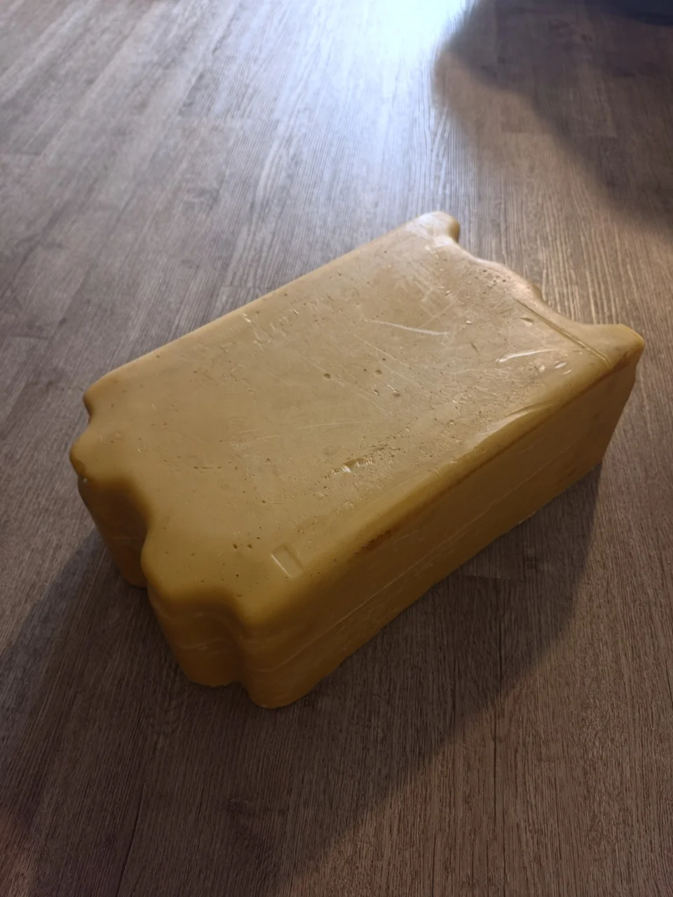 A large yellow beeswax block on a wooden surface.