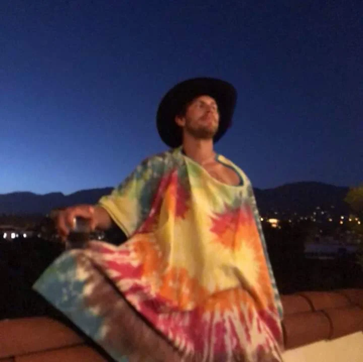 Shiva outdoors at dusk, wearing a black hat and a colorful poncho.
